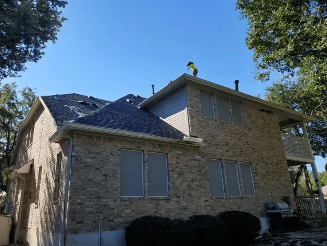 Two-story brick house with new roof. Person on roof. Blue sky.