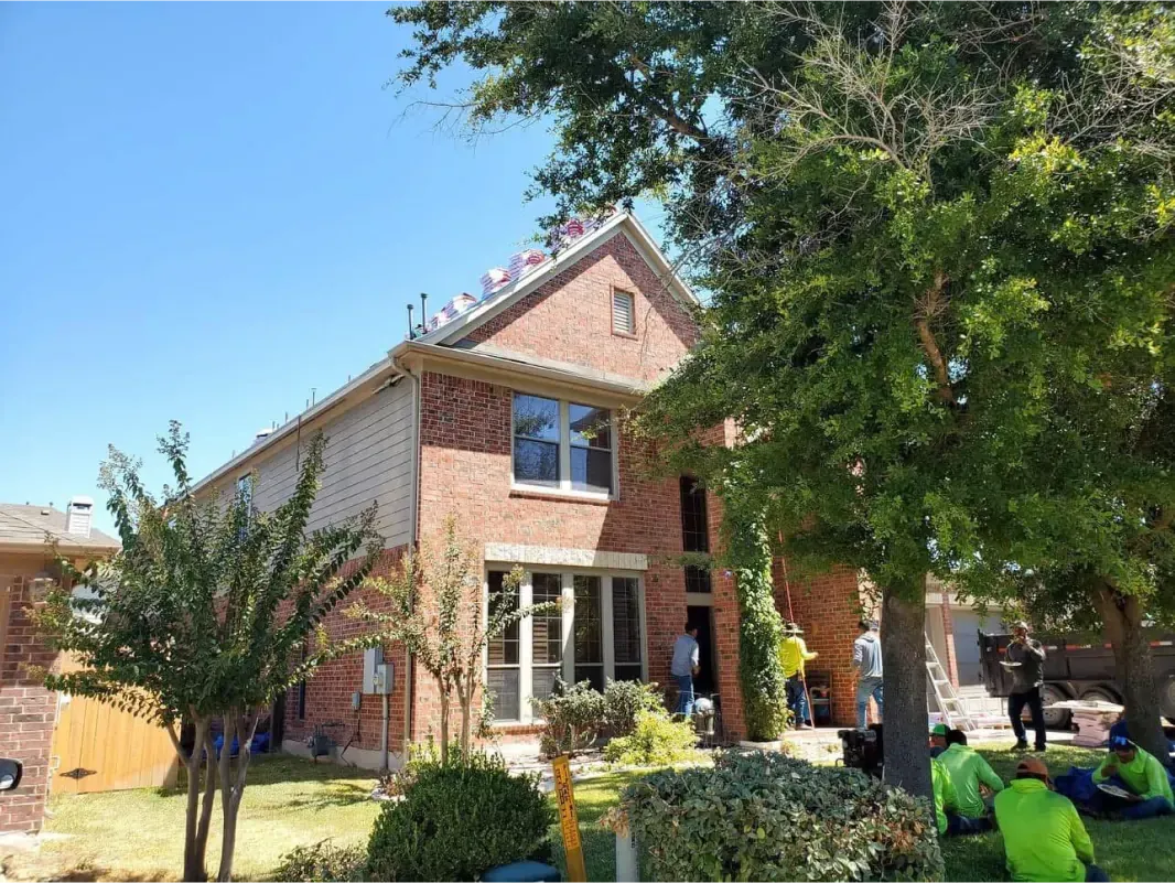 Brick house under construction, workers, blue sky, trees, green grass.