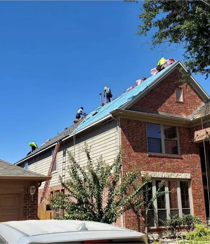 Roofers working on a two-story brick and siding house under a clear blue sky.