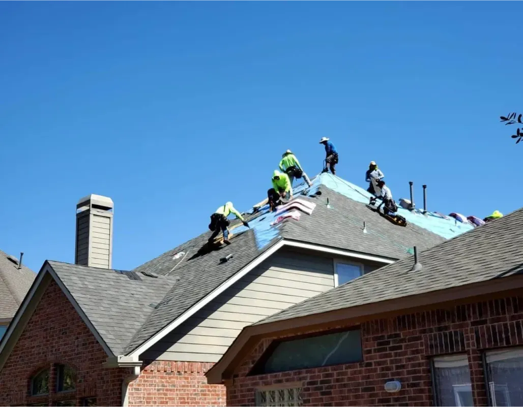 Roofers installing shingles on a residential home with a clear blue sky.