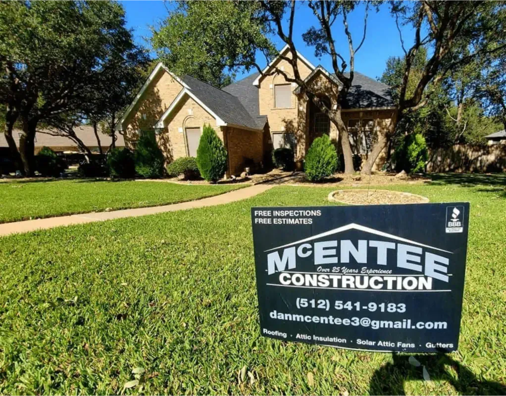 Sign for McEntee Construction in front of a two-story brick home with a green lawn.