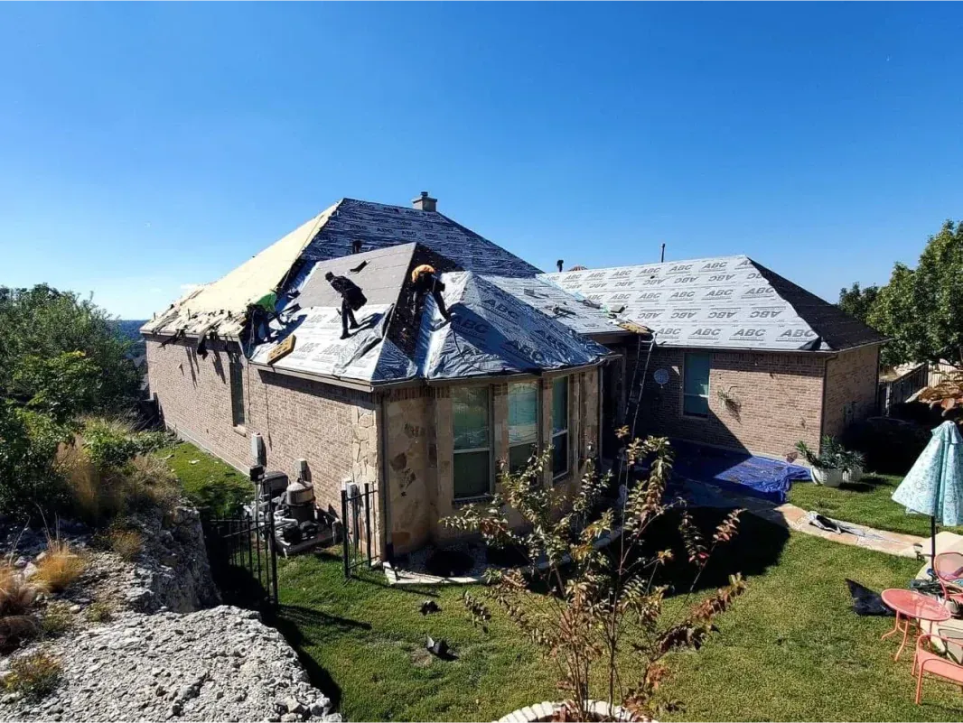 Workers on a house roof, partially covered in new shingles. Sunny day.