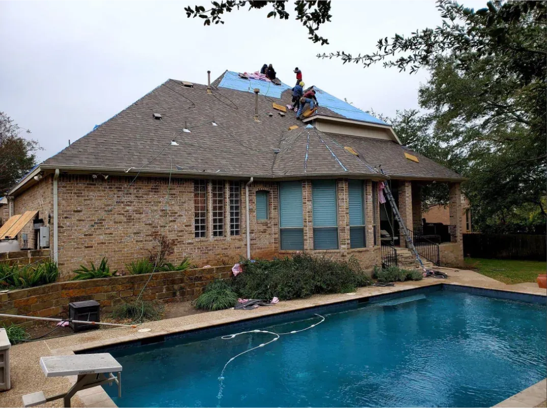 Roofers working on a house with a brick exterior, overlooking a swimming pool.