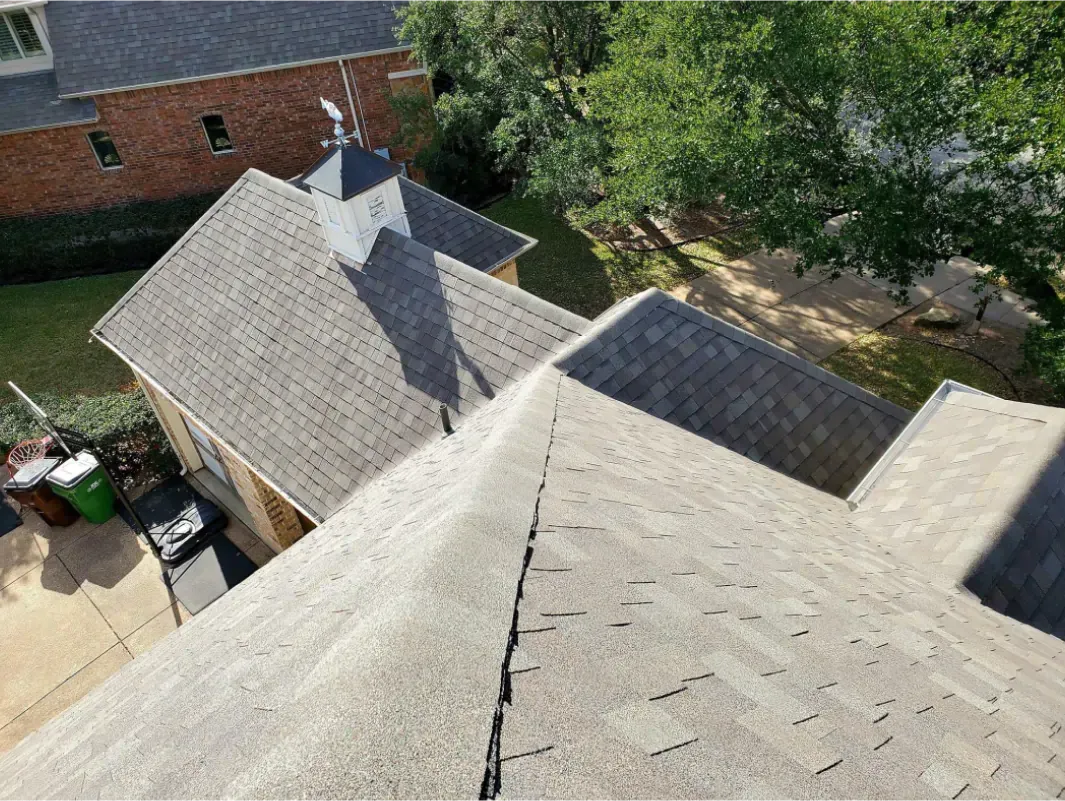 Overhead view of a grey shingled roof with a small steeple, residential neighborhood setting.