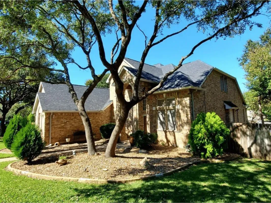 Tan brick house with gray roof, tree in front, blue sky.