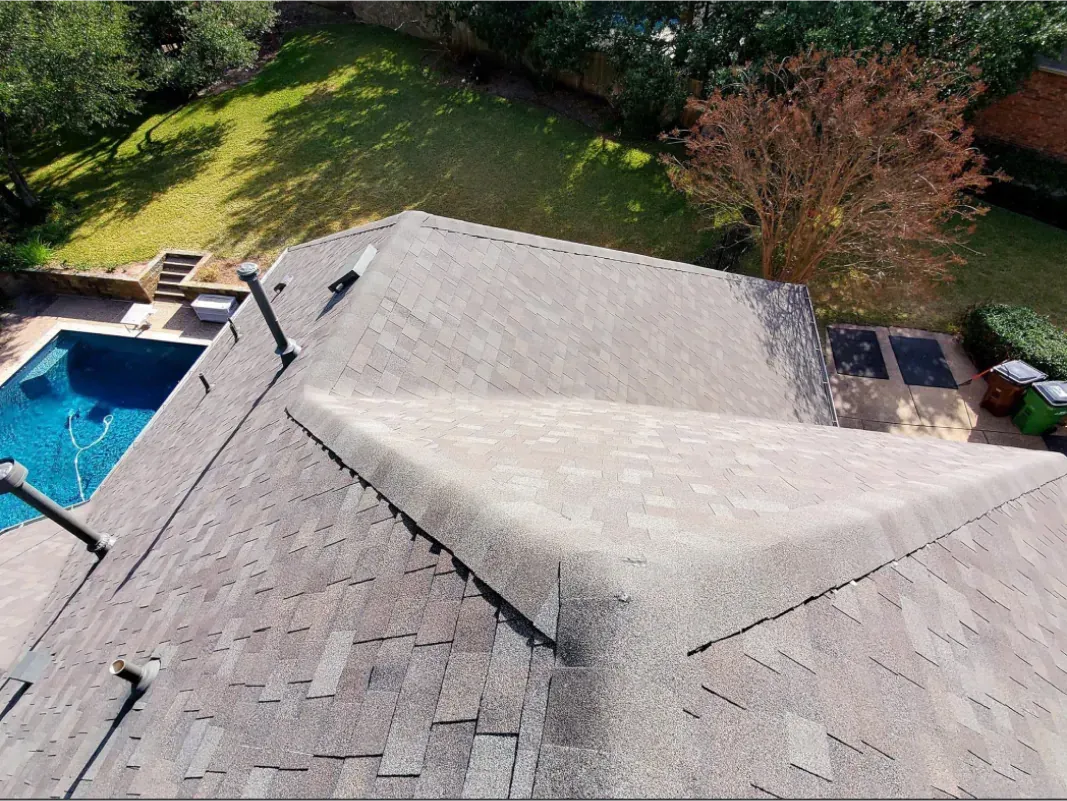 Overhead view of a house roof, part of a backyard with a pool, trees, and grass.