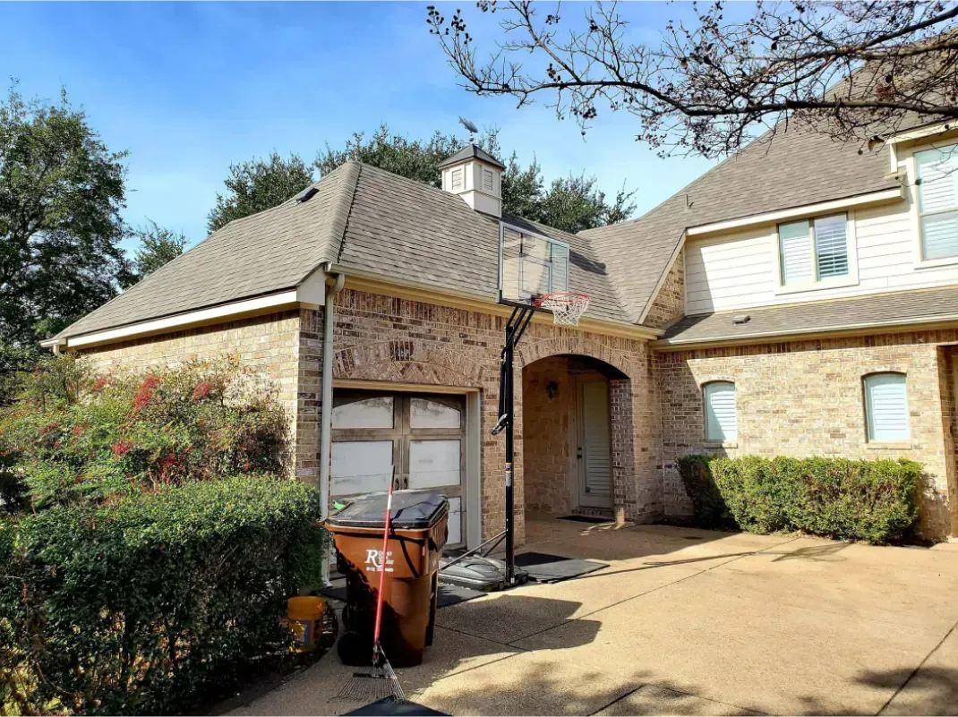 A two-story brick house with a garage. Brown trash bin sits in the driveway.