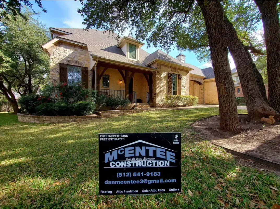 House with stone facade, arched entry, and landscaping. A McEntee Construction sign is in the front yard.
