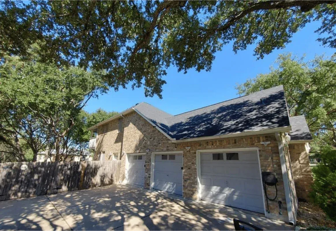 Stone garage with three doors, gray doors, and black roof, under a blue sky and leafy trees.