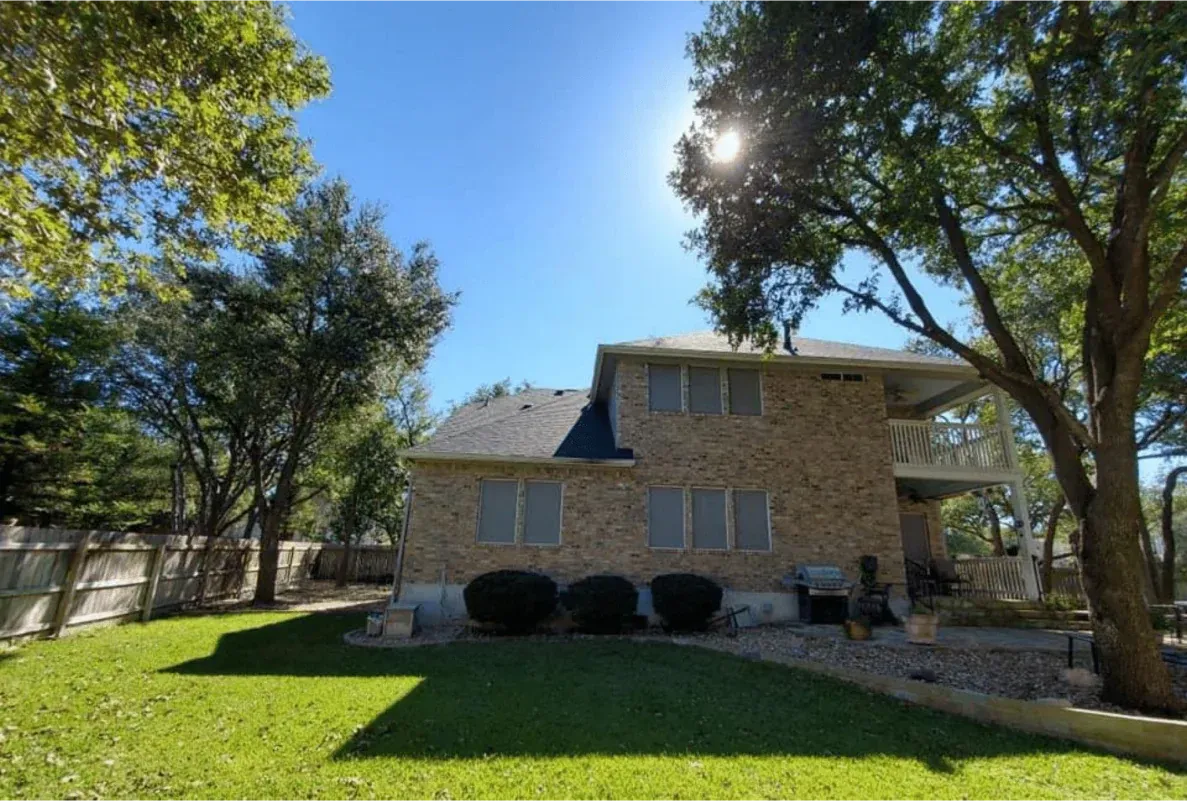 Two-story brick house with green lawn and trees under a bright blue sky.