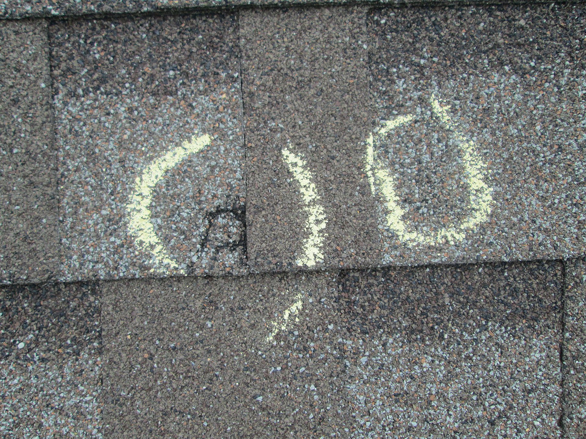 A shingled roof surface with yellow chalk circles marking two spots, one containing the hand-written letter