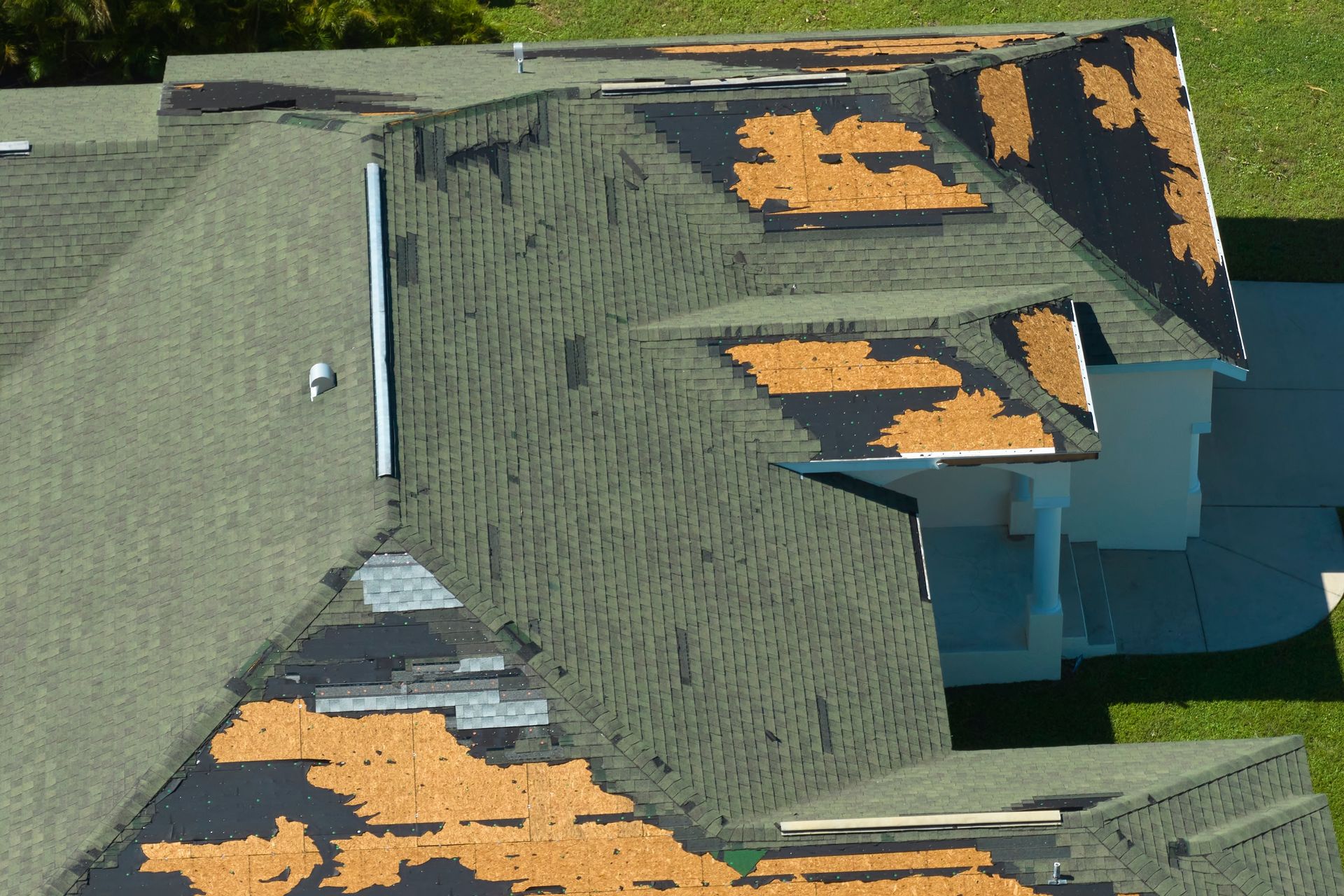 An aerial view of a residential roof with missing and damaged shingles, exposing the underlying roofing material.