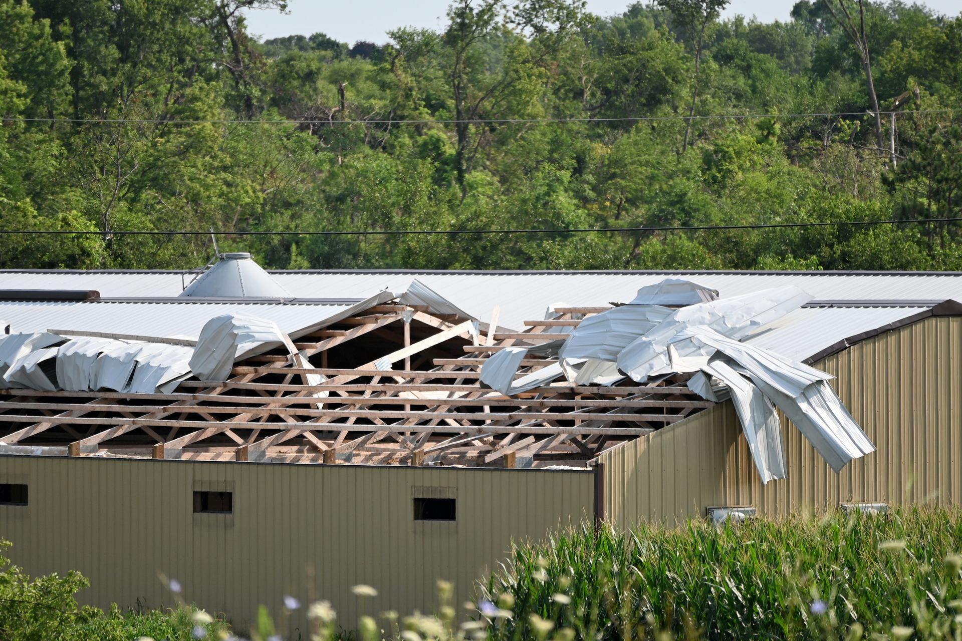 Damaged building with exposed wooden roof frame; metal roofing torn off.