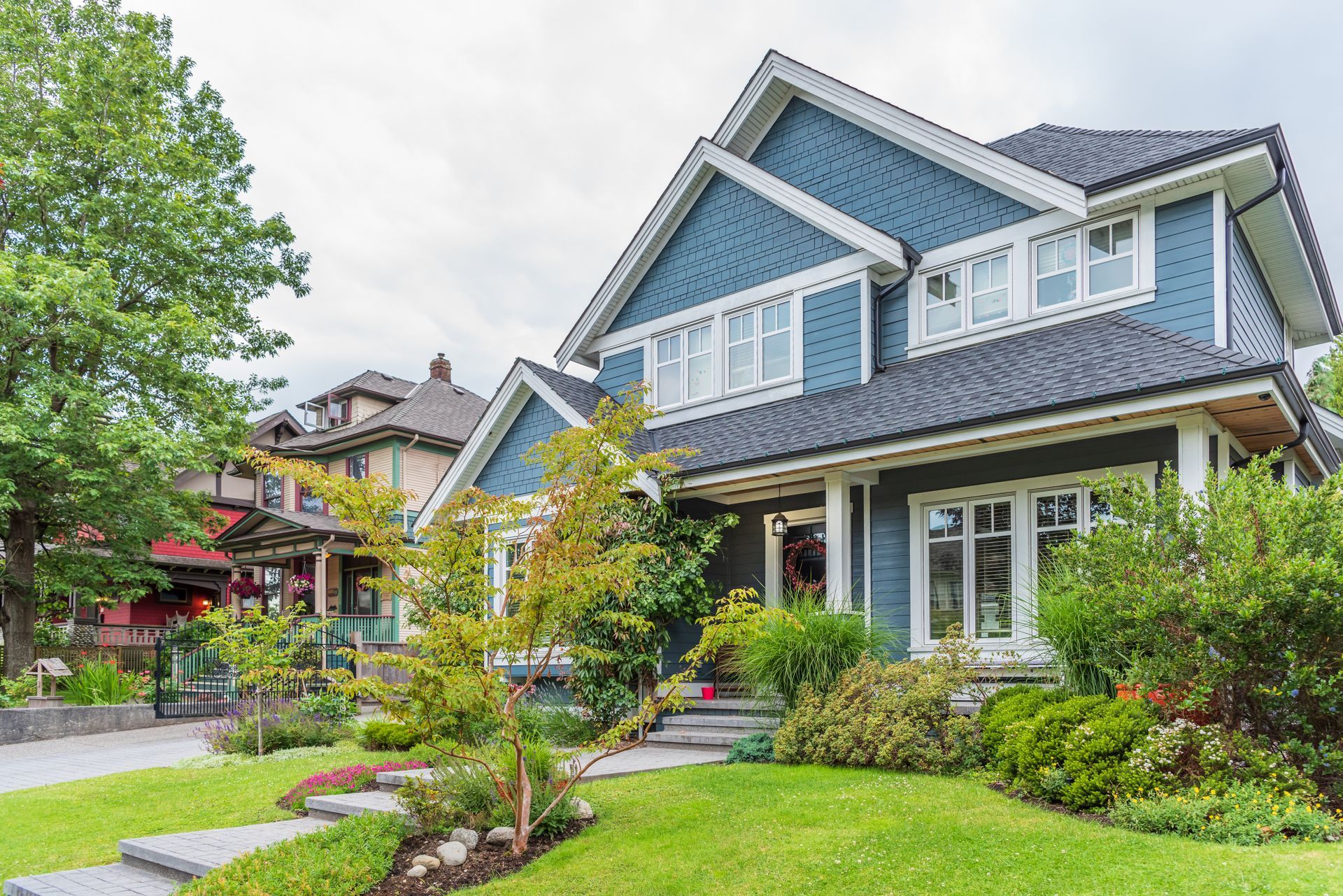 Blue two-story house with white trim and a black roof, set on a green lawn with a stone path.