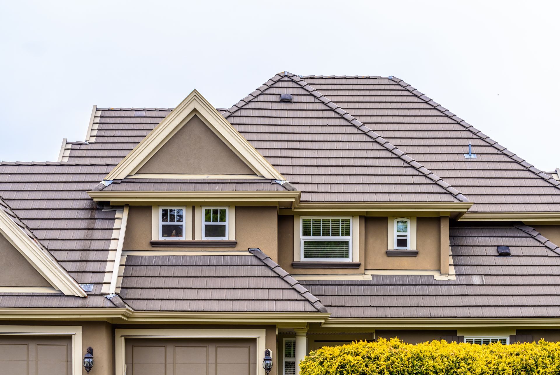 Tan stucco house with brown tile roof, multiple gables, and small windows.
