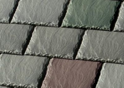 Slate roof tiles, varying shades of gray and green, overlapping in a pattern.
