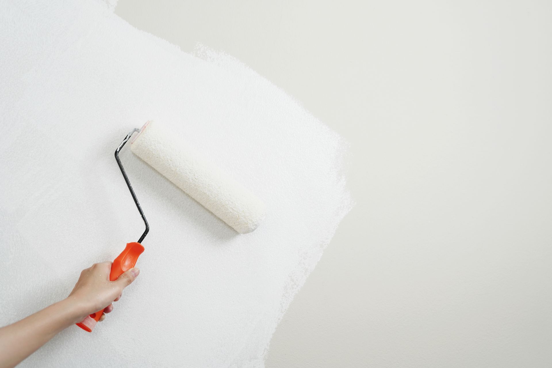 Painter on scaffolding rolling gray paint onto a building's wall.