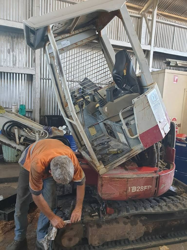 Man Working on a Red and White Kubota Excavator in a Garage — RCM Diesel & Hydraulic Services in West Rockhampton, QLD