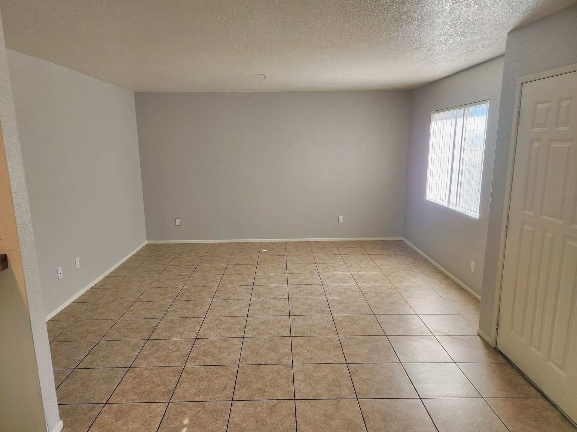 An empty living room with a tiled floor and a window.