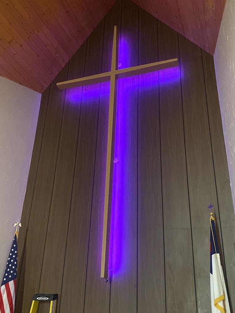 A large wooden cross with a purple light behind it in a church.