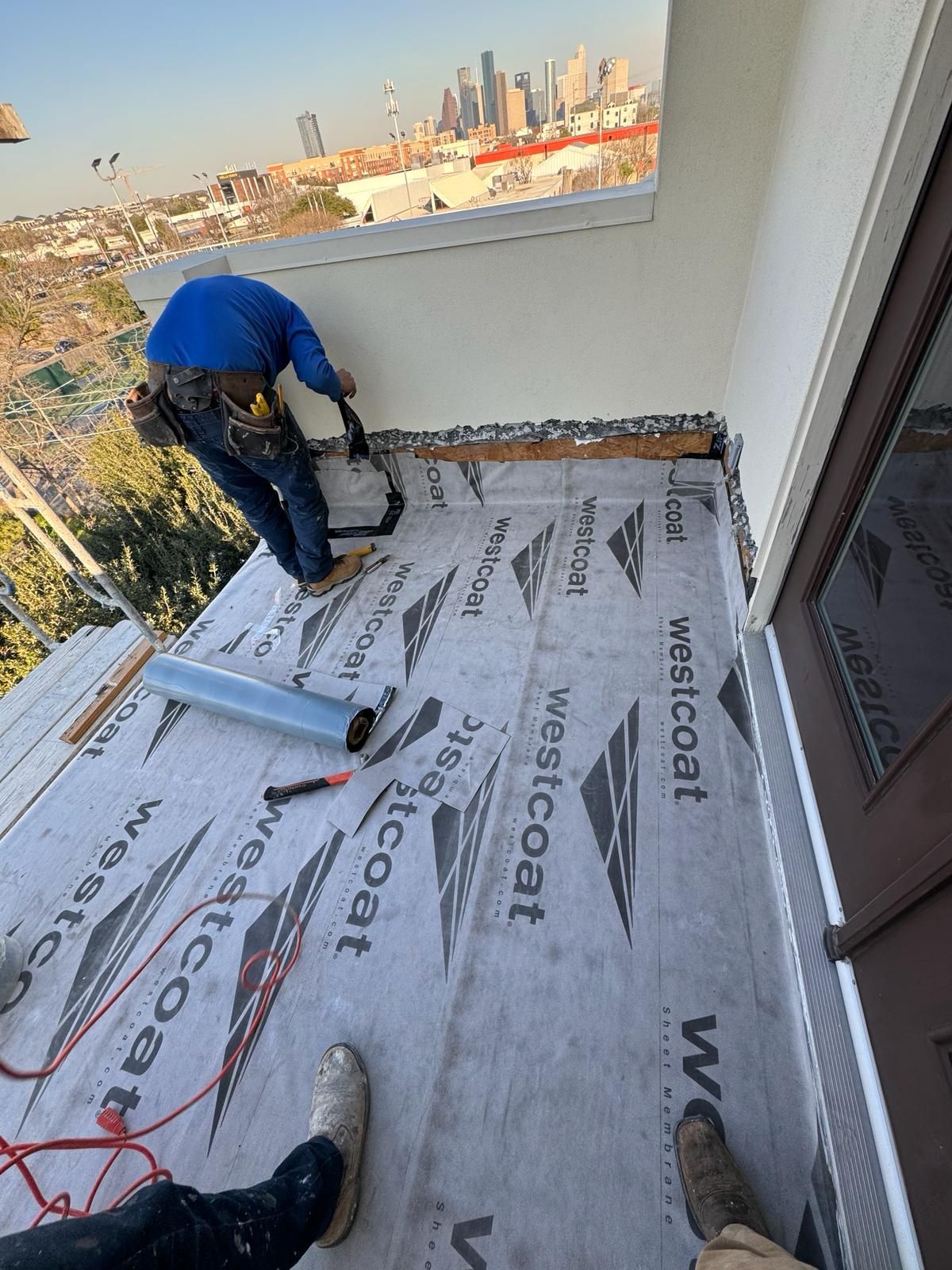 A man is working on a roof with a city in the background.