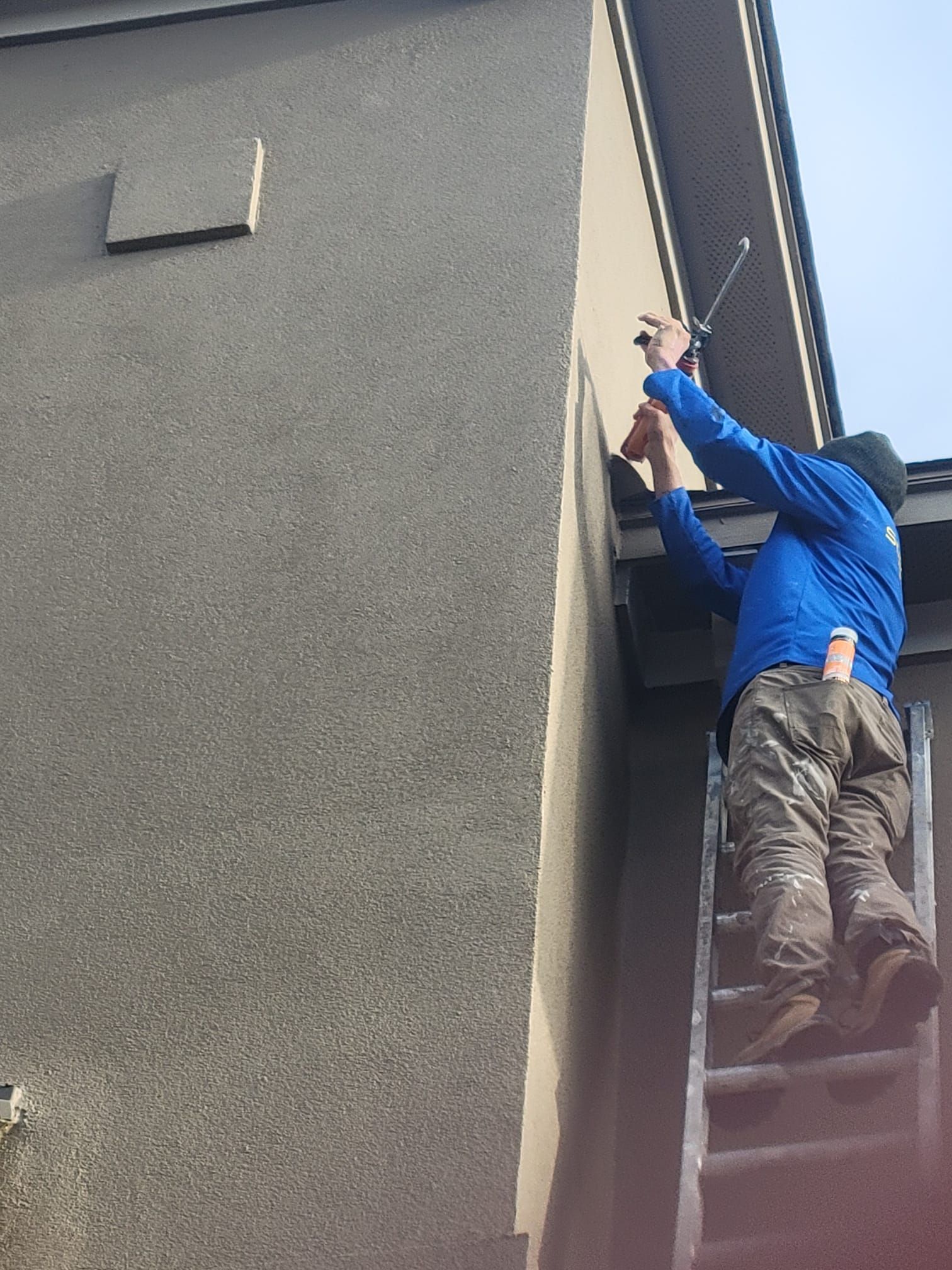A man is standing on a ladder on the side of a building.