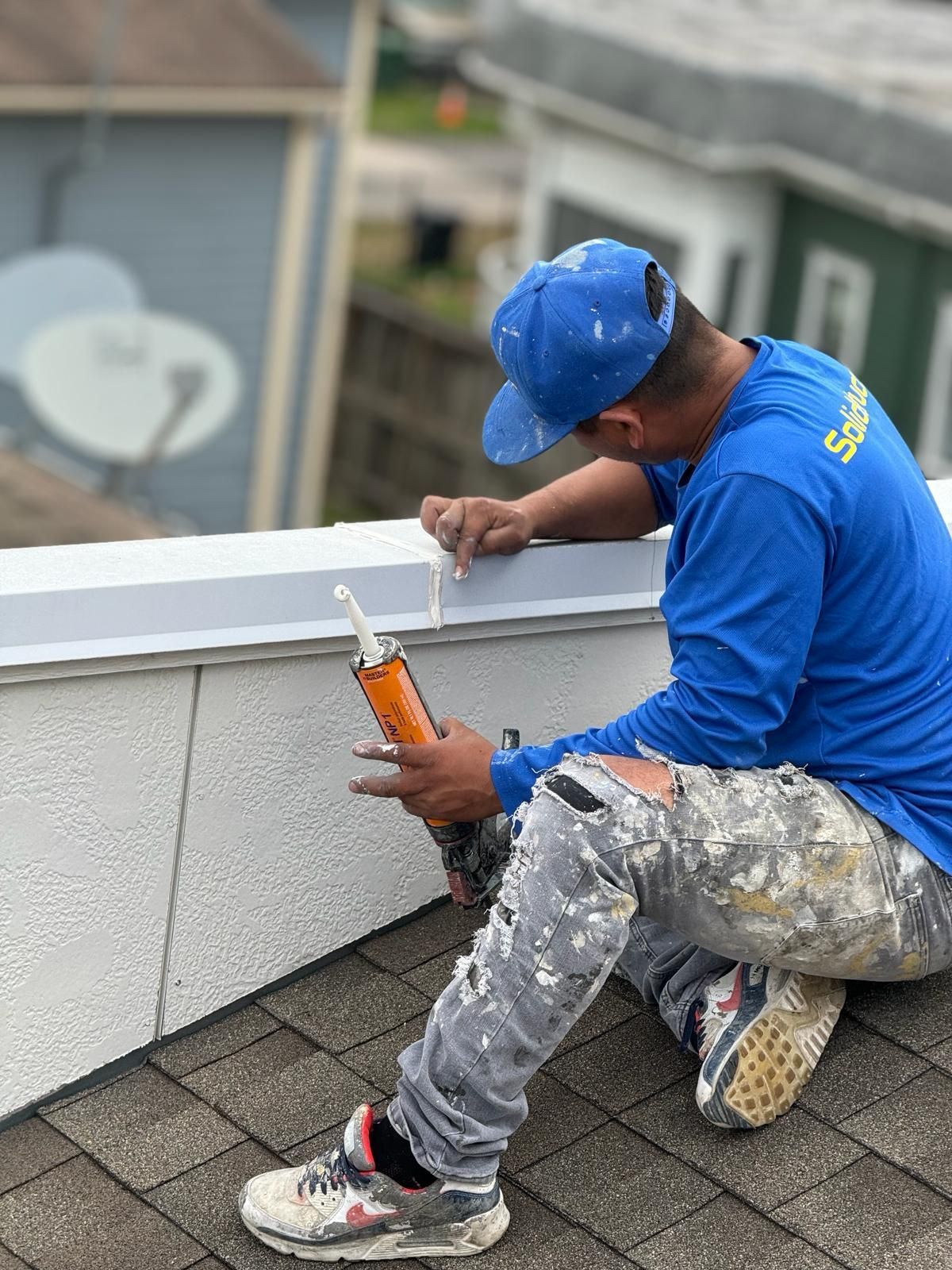 A man is sitting on the roof of a building holding a bottle of sealant.