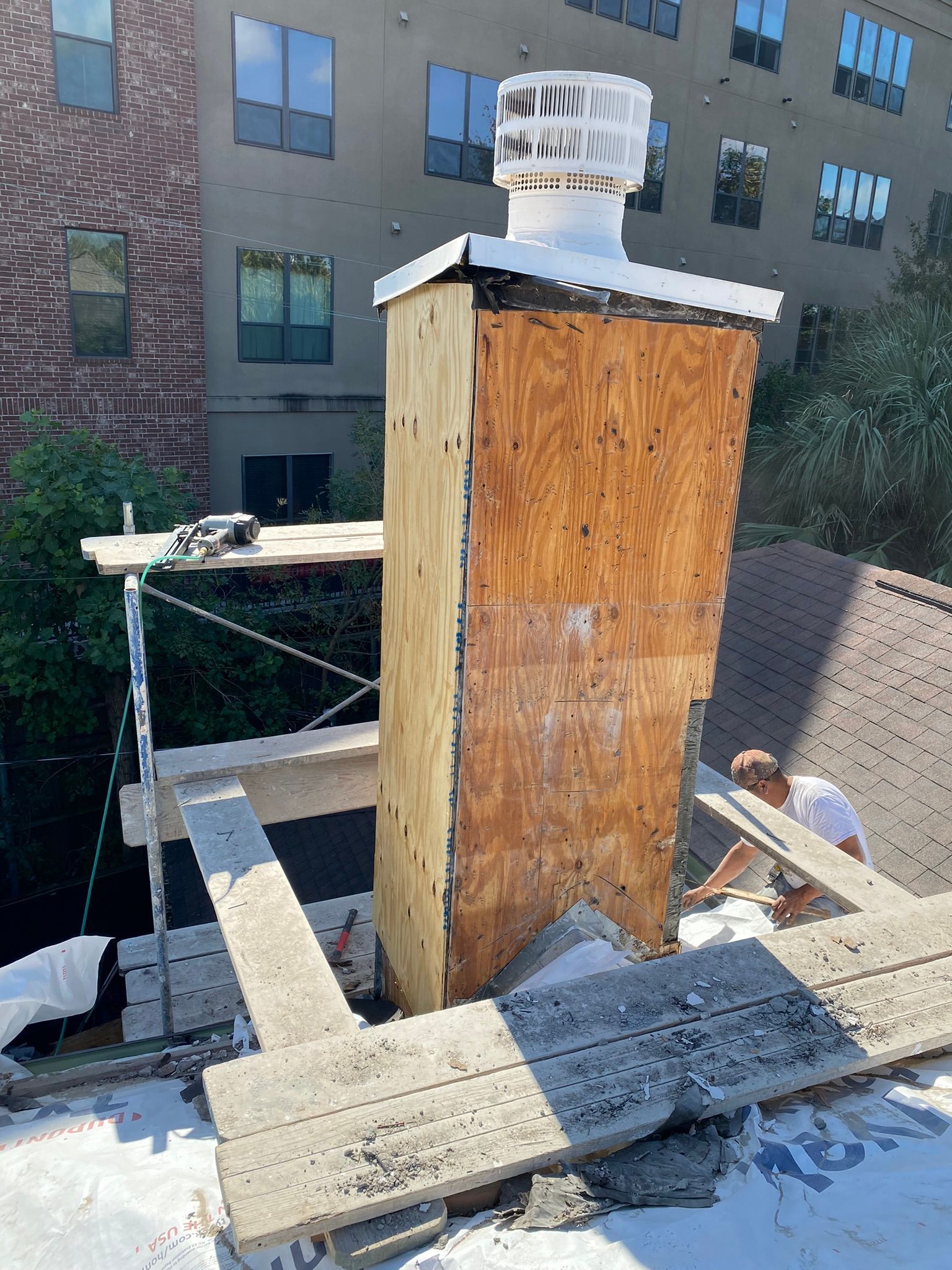 A man is working on a chimney on the roof of a building.