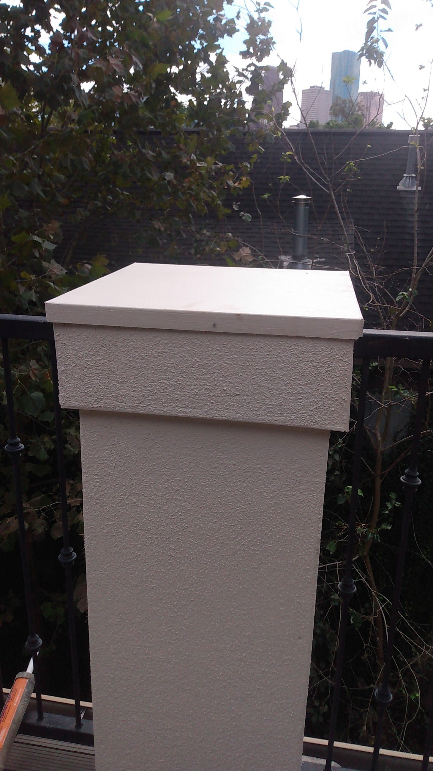 A white pillar with a black railing and trees in the background.