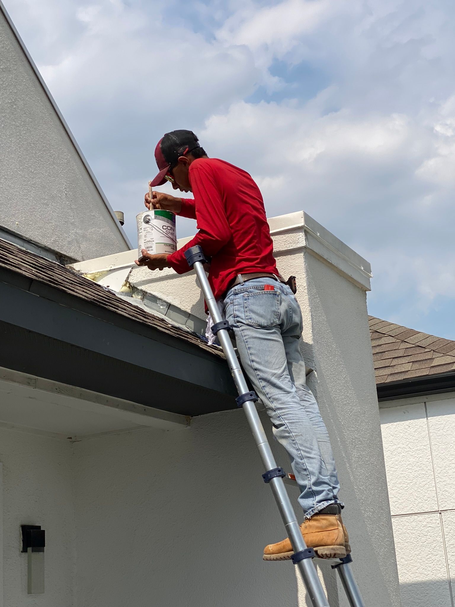 A man is standing on a ladder painting the side of a building.
