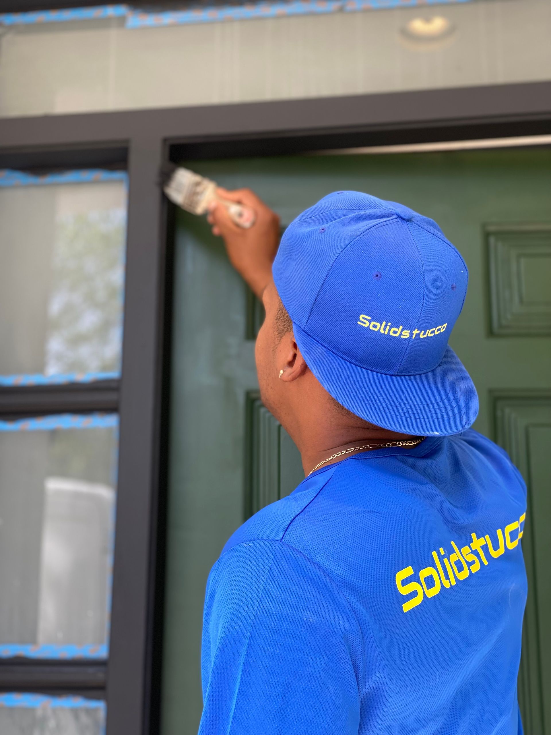 A man in a blue shirt is painting a door with a brush.