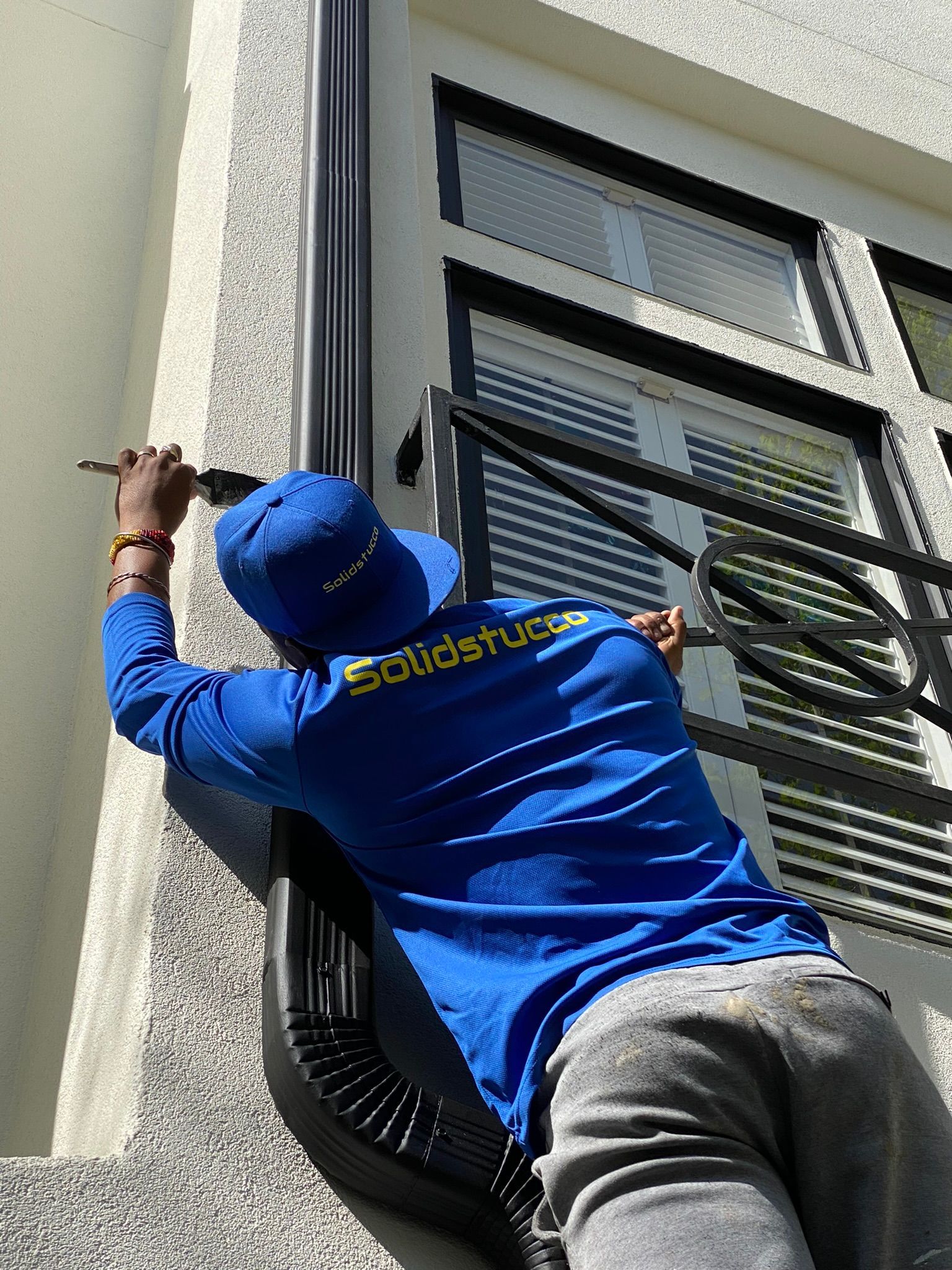 A man in a blue shirt is painting a window on a building.