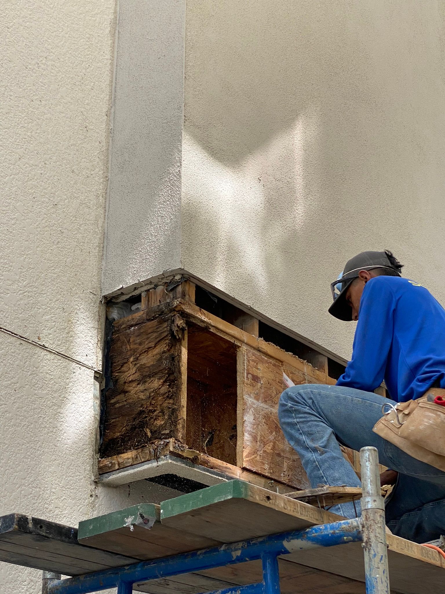 A man is sitting on a scaffolding working on a wall.
