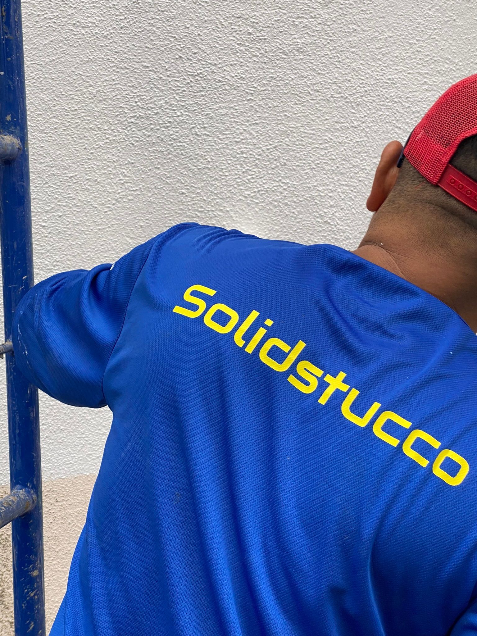 A man wearing a blue shirt and a red hat is working on a wall.