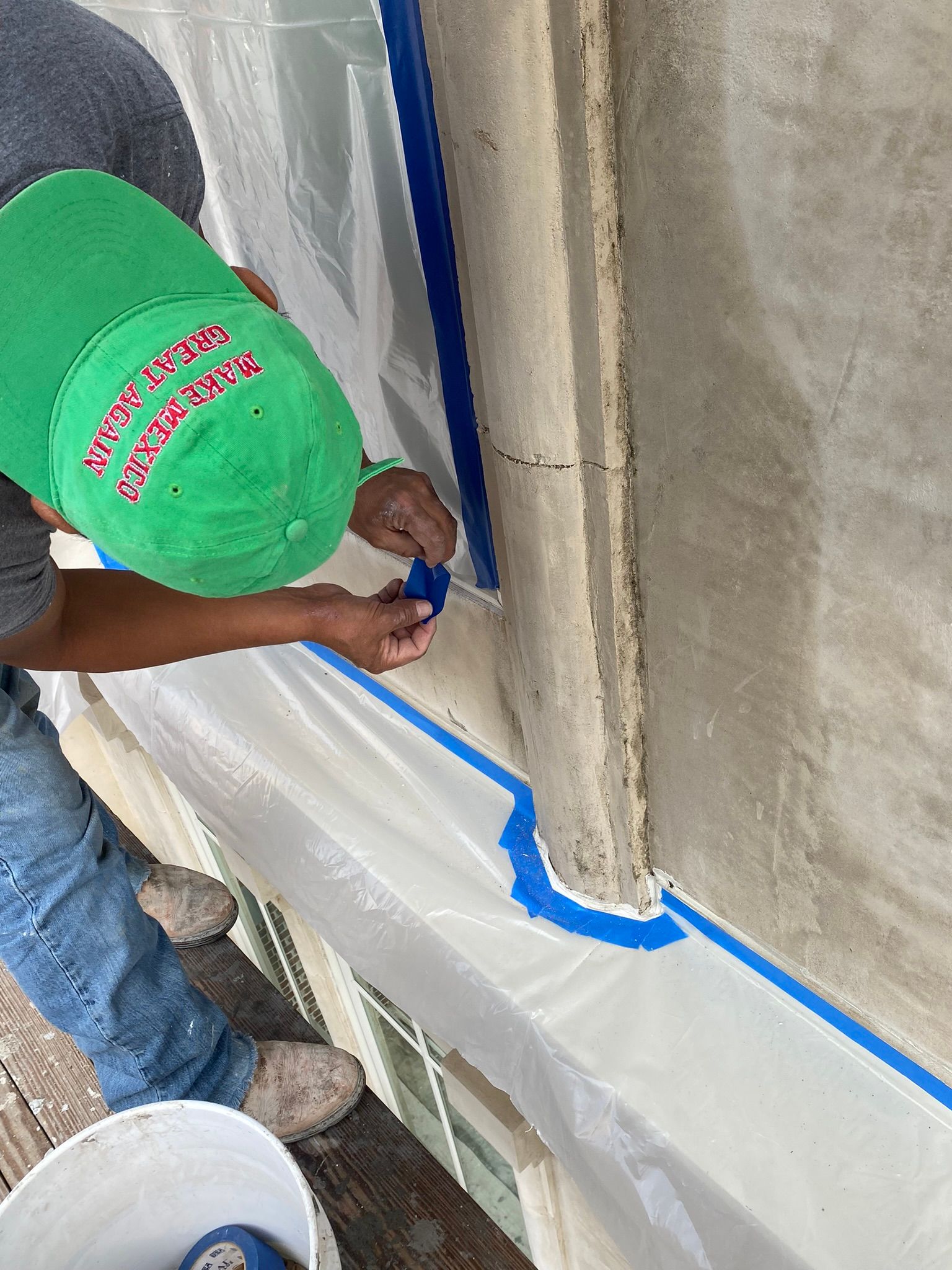 A man wearing a green hat is painting a wall.