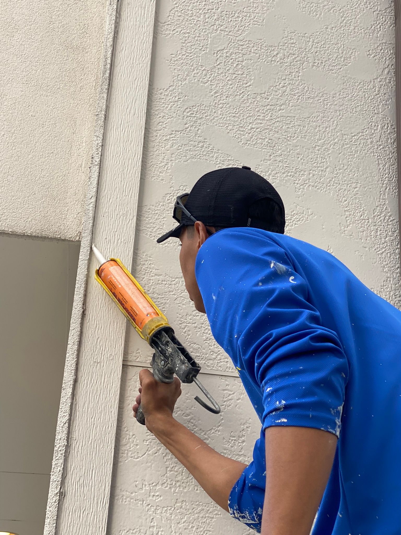A man in a blue shirt is applying silicone to a wall.