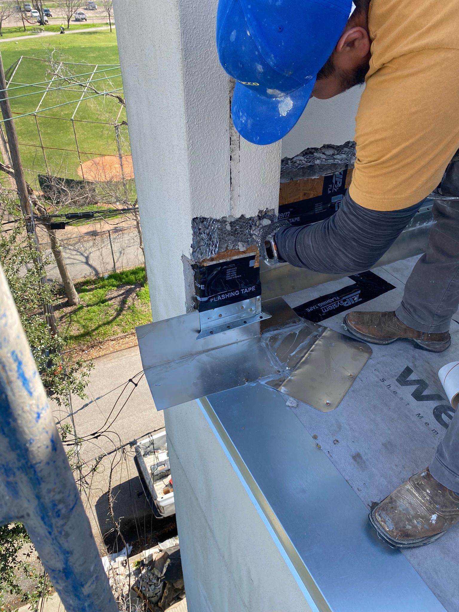 A man wearing a blue hard hat is working on the side of a building.