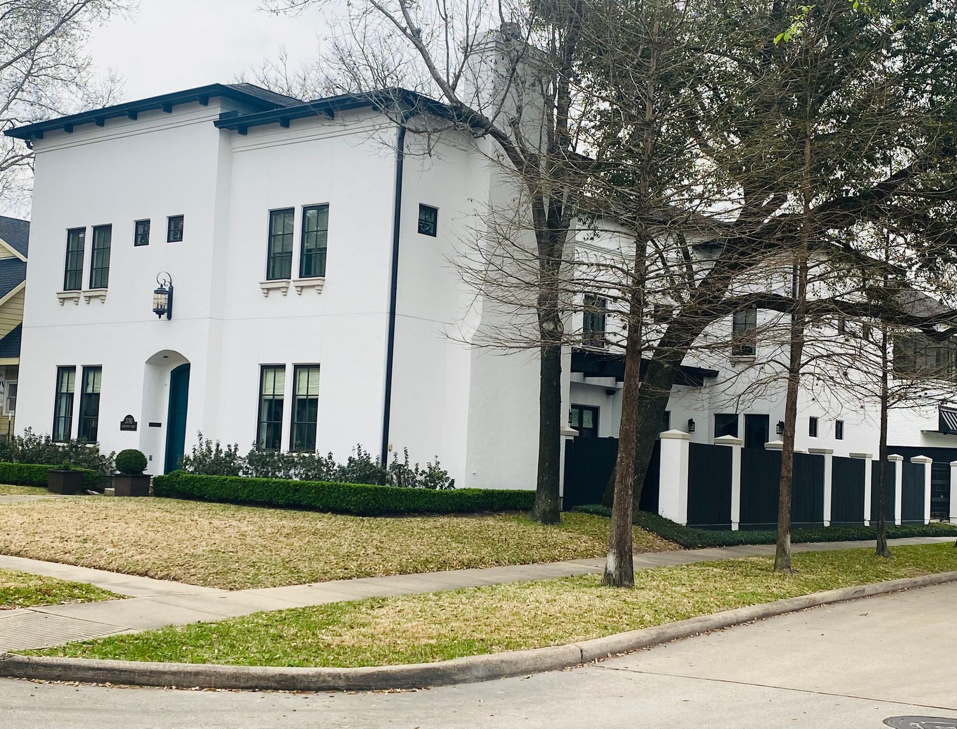 A white house with a black fence and trees in front of it