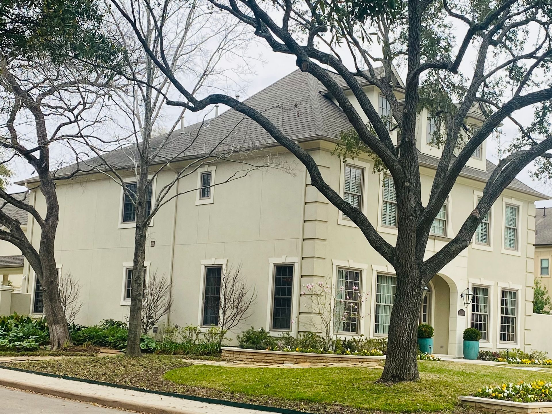 A large white house with a gray roof and trees in front of it.