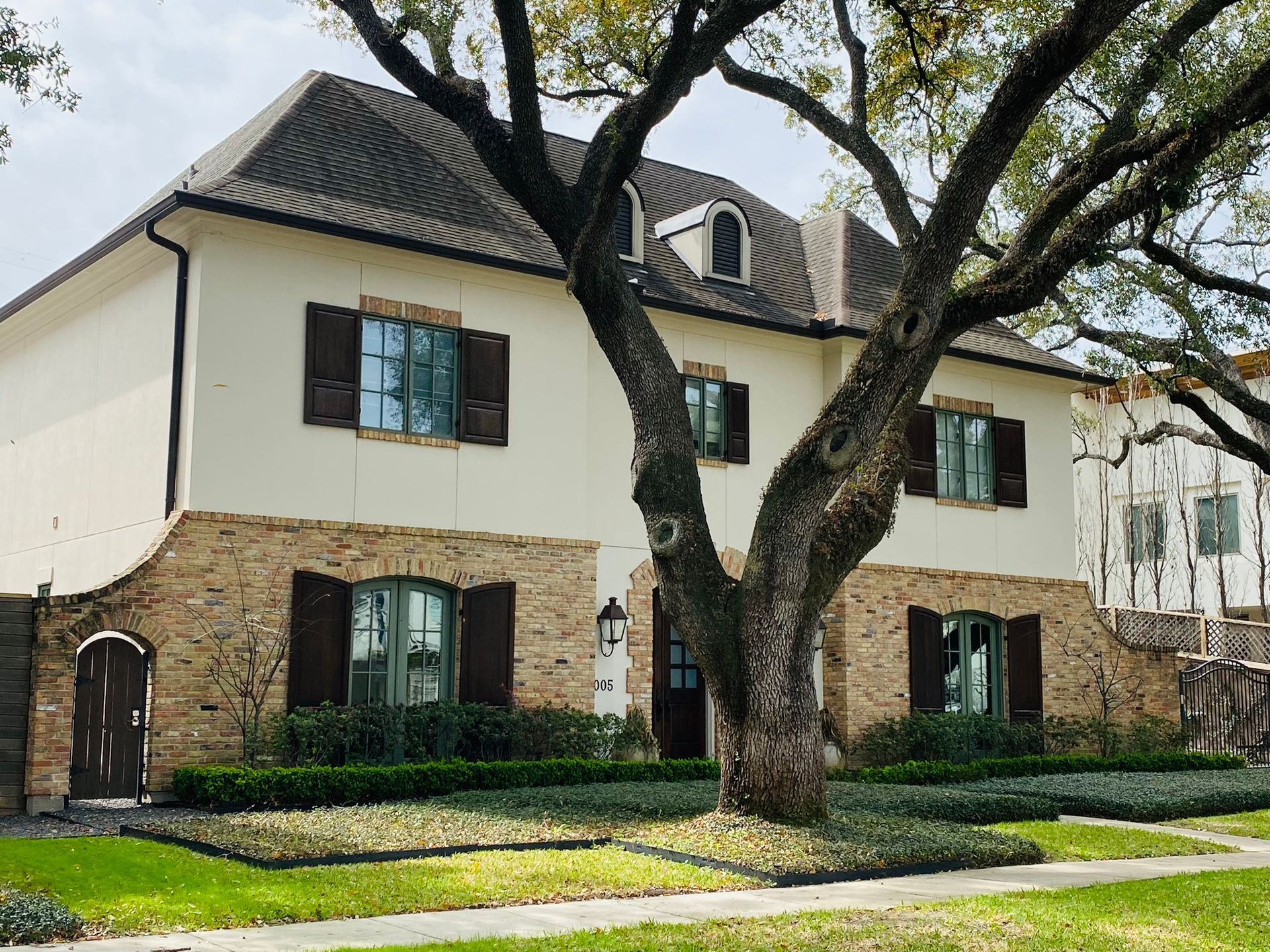A large white house with brown shutters and a tree in front of it.