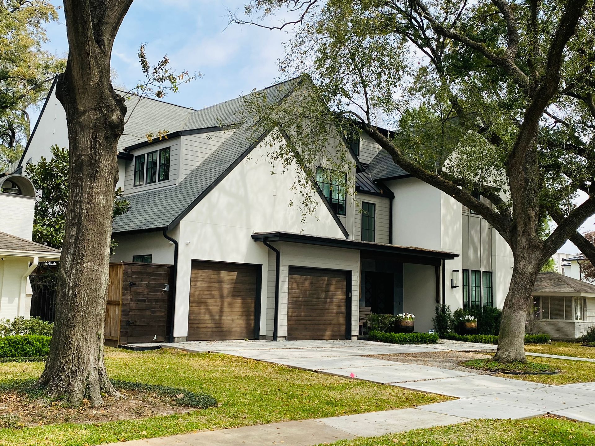 A large white house with three garage doors is surrounded by trees.