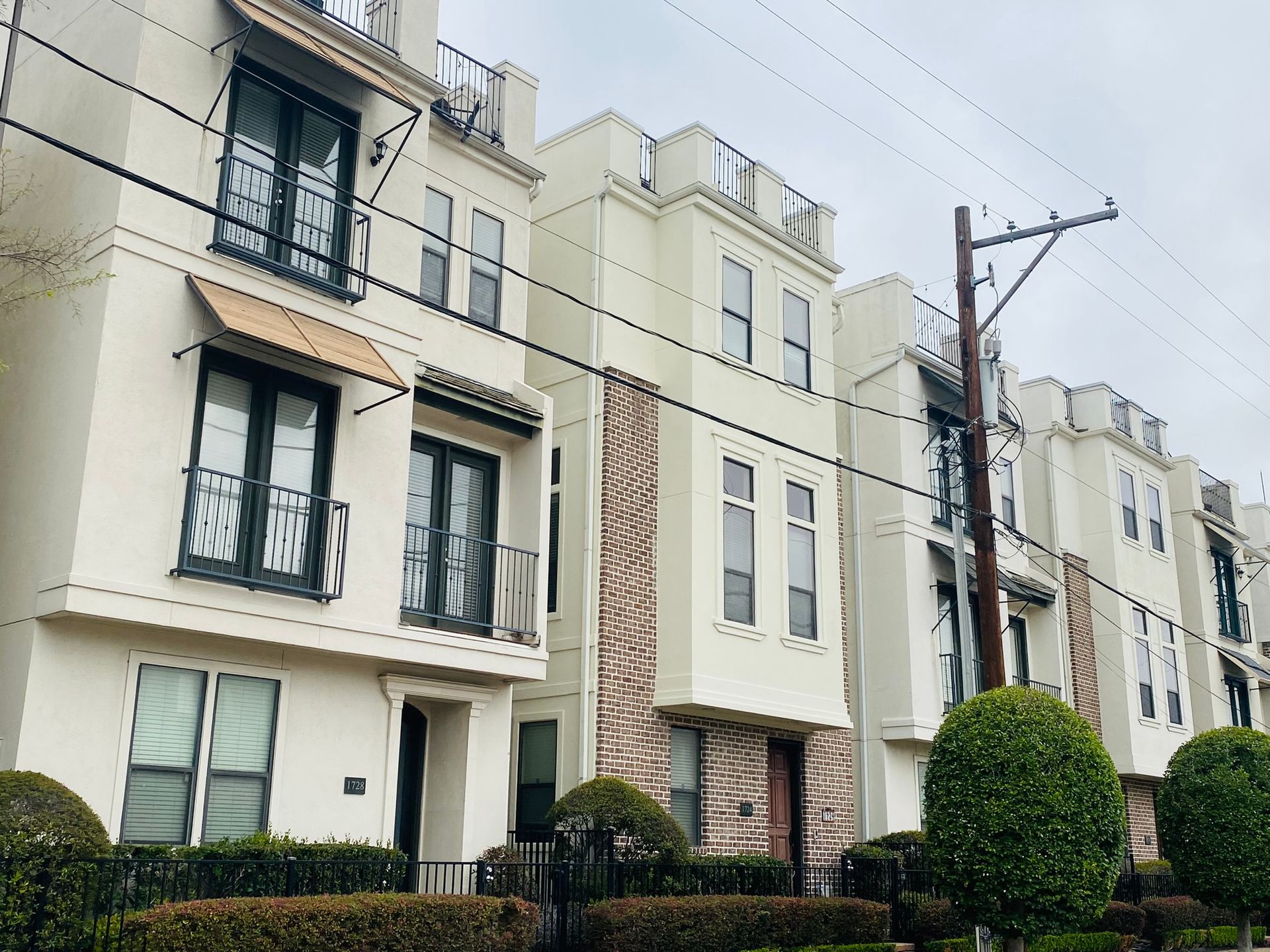 A row of white apartment buildings with balconies and trees in front of them