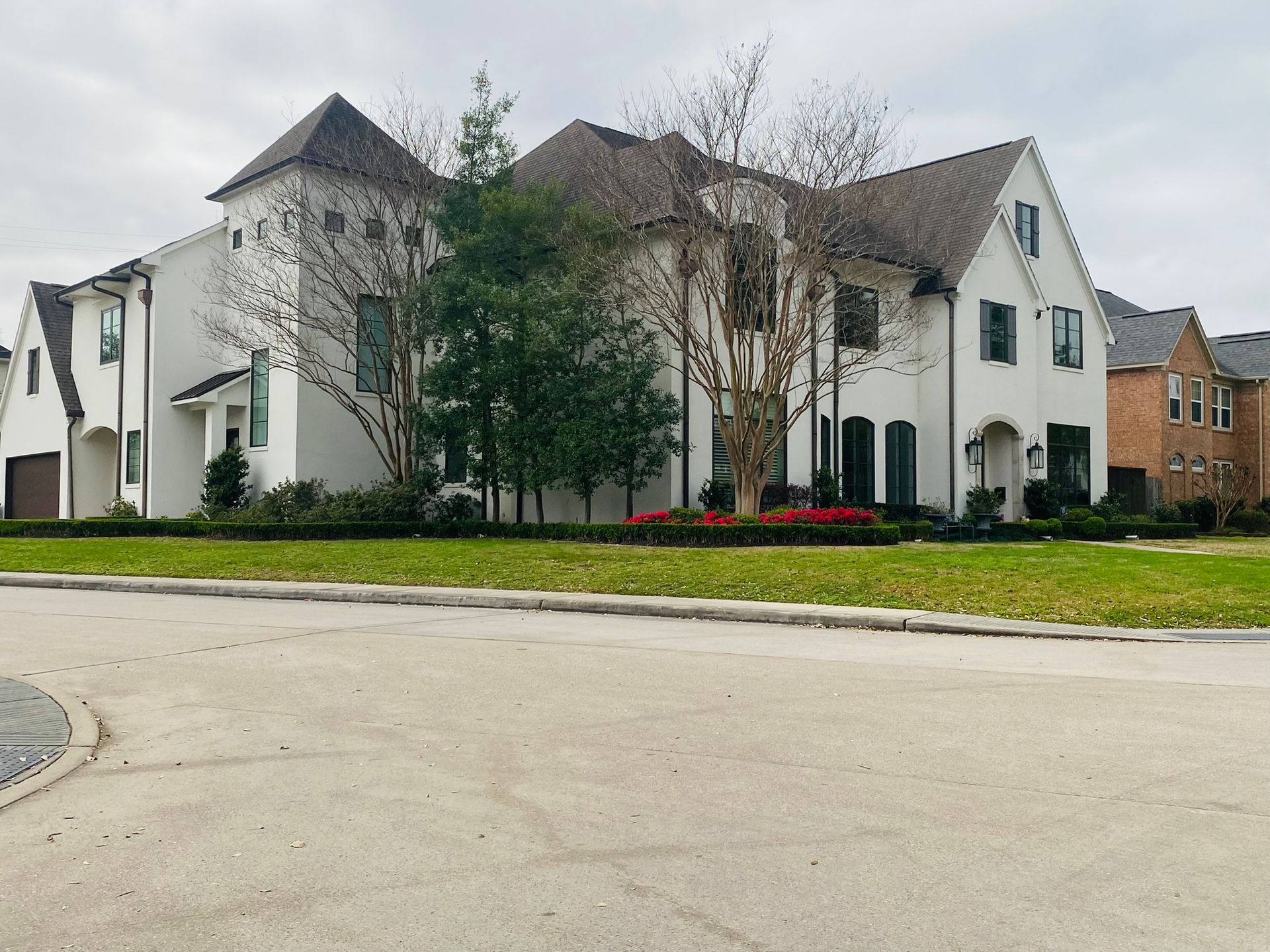 A large white house with a brown roof is sitting on top of a lush green field.