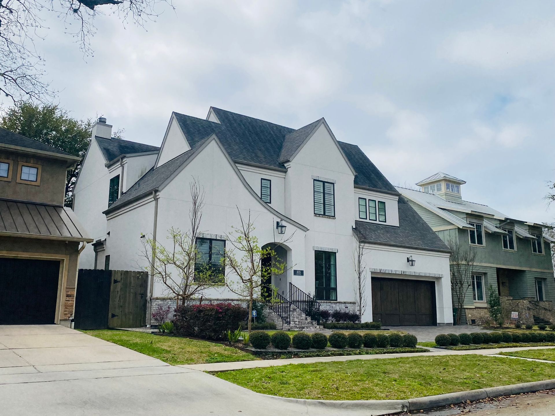 A large white house with a black roof is sitting on the corner of a street.