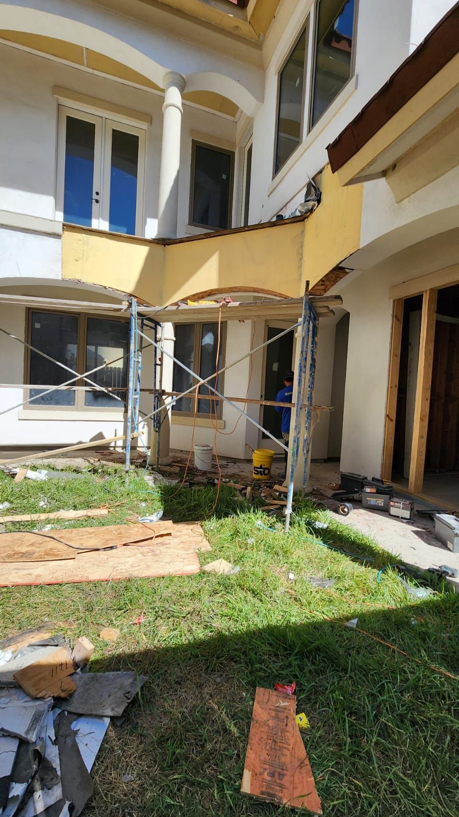 A large white house is being remodeled with scaffolding in the backyard.