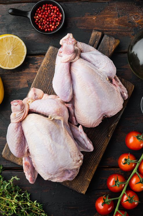 Two raw chickens are sitting on a wooden cutting board.