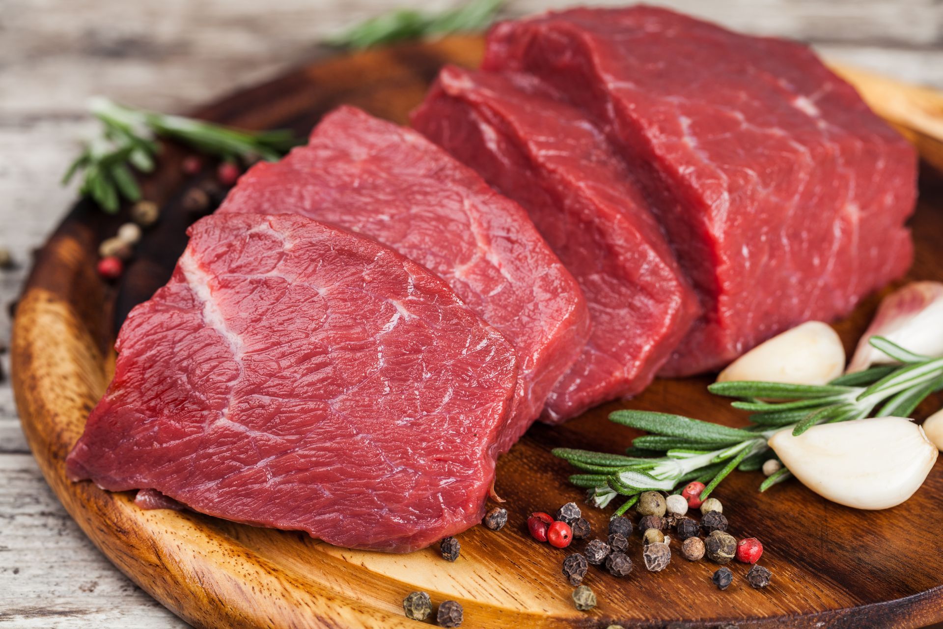 Raw beef steaks on a wooden cutting board with spices.