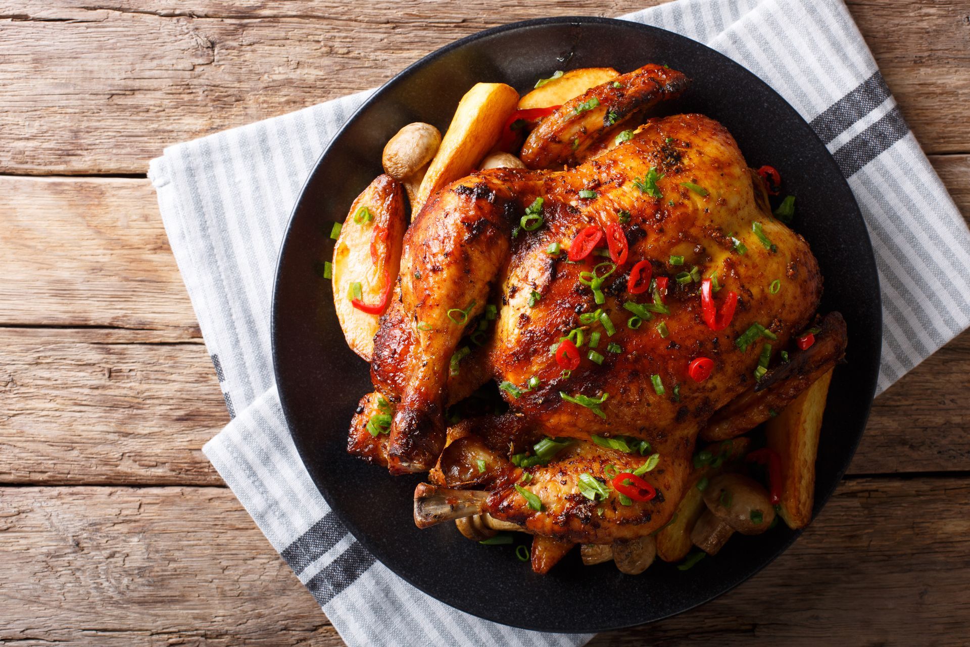 A black plate topped with roasted chicken and potatoes on a wooden table.