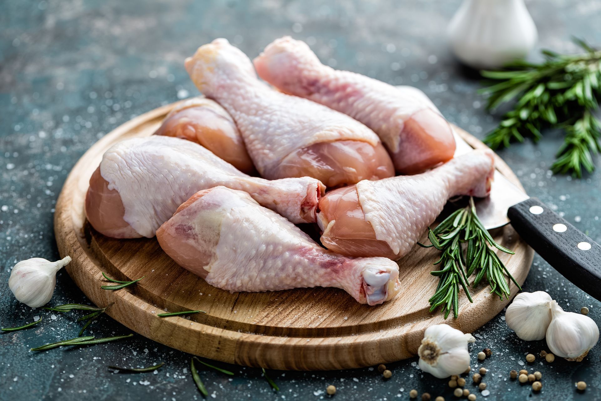 Raw chicken legs on a wooden cutting board with garlic and rosemary.