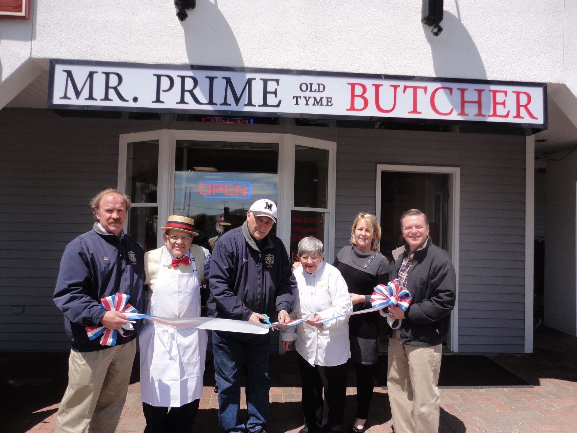 A group of people cutting a ribbon in front of mr. prime old tyme butcher